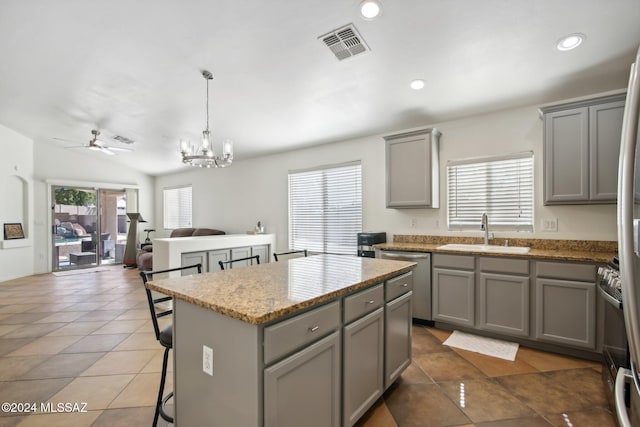 kitchen featuring a center island, light stone countertops, sink, gray cabinets, and pendant lighting