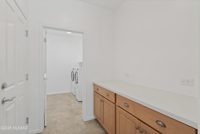 clothes washing area with washing machine and clothes dryer, baseboards, and light tile patterned floors