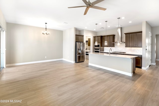 kitchen featuring wall chimney range hood, appliances with stainless steel finishes, pendant lighting, light hardwood / wood-style floors, and sink