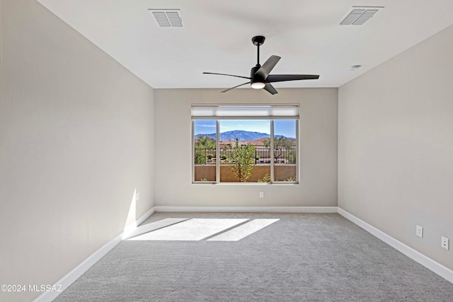 spare room with a mountain view, light colored carpet, and ceiling fan