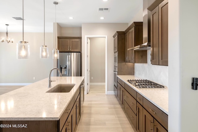 kitchen featuring a center island with sink, hanging light fixtures, light stone countertops, sink, and stainless steel appliances