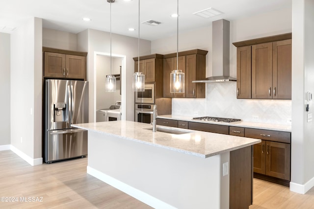 kitchen featuring wall chimney range hood, appliances with stainless steel finishes, light stone countertops, sink, and decorative light fixtures