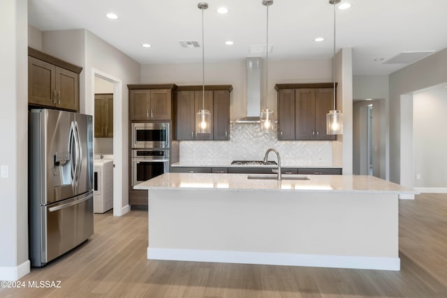 kitchen with a kitchen island with sink, wall chimney exhaust hood, appliances with stainless steel finishes, and hanging light fixtures