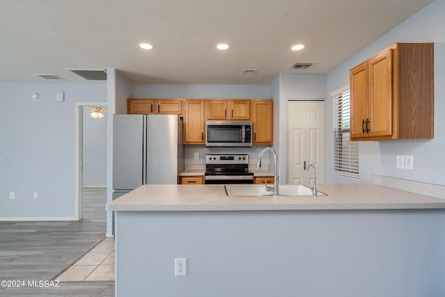 kitchen with appliances with stainless steel finishes, kitchen peninsula, sink, and light hardwood / wood-style floors