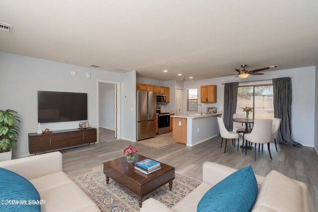 living room with ceiling fan, sink, and light wood-type flooring