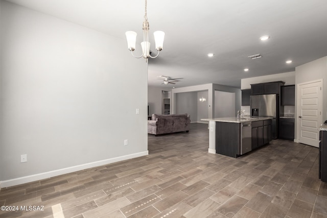 kitchen with light stone counters, appliances with stainless steel finishes, dark wood-type flooring, ceiling fan with notable chandelier, and sink