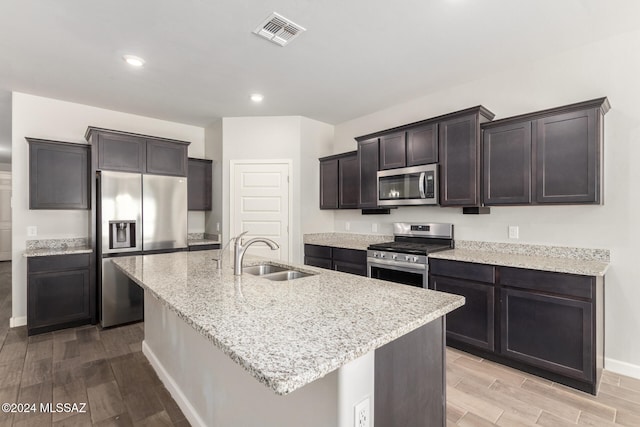 kitchen with dark brown cabinets, an island with sink, appliances with stainless steel finishes, light hardwood / wood-style floors, and sink