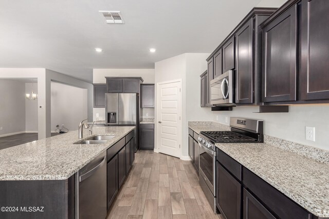 kitchen with a kitchen island with sink, light hardwood / wood-style flooring, sink, appliances with stainless steel finishes, and light stone counters