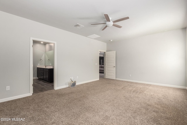 unfurnished bedroom with dark colored carpet, ensuite bathroom, and ceiling fan