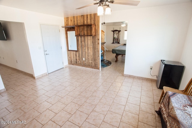 unfurnished room featuring light tile patterned floors, ceiling fan, and wood walls