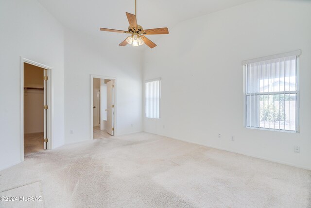 carpeted empty room featuring ceiling fan, high vaulted ceiling, and a wealth of natural light