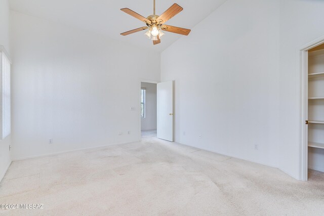 unfurnished bedroom featuring a high ceiling, ensuite bath, a spacious closet, light colored carpet, and ceiling fan