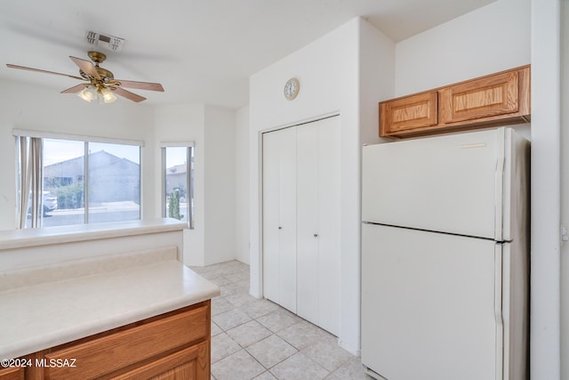 kitchen with light tile patterned floors, a ceiling fan, freestanding refrigerator, light countertops, and brown cabinets