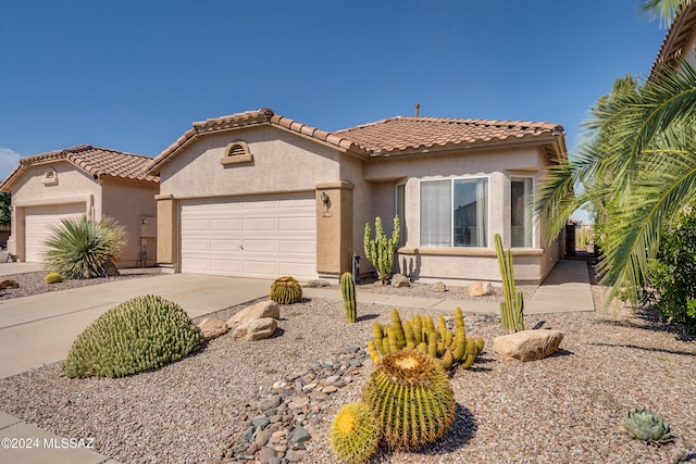 mediterranean / spanish-style house featuring a tiled roof, stucco siding, an attached garage, and driveway