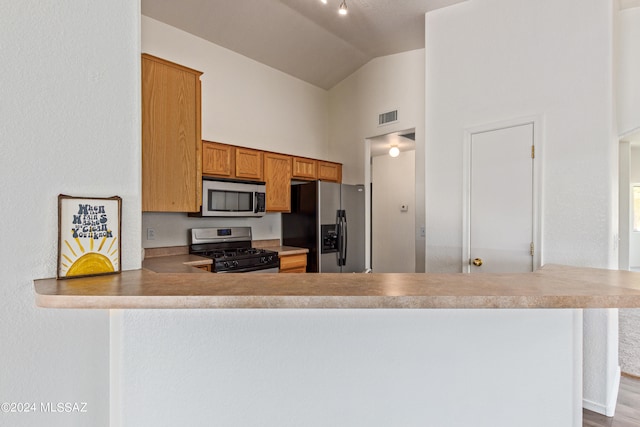 kitchen featuring wood-type flooring, appliances with stainless steel finishes, lofted ceiling, and kitchen peninsula