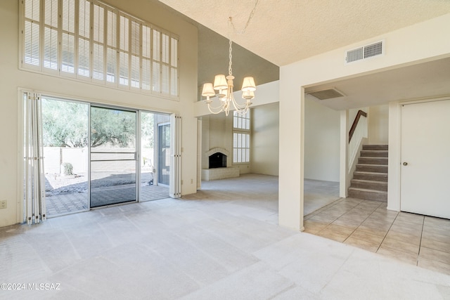 unfurnished living room with a towering ceiling, an inviting chandelier, carpet floors, and a textured ceiling