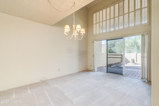 carpeted empty room with a towering ceiling, an inviting chandelier, and a textured ceiling