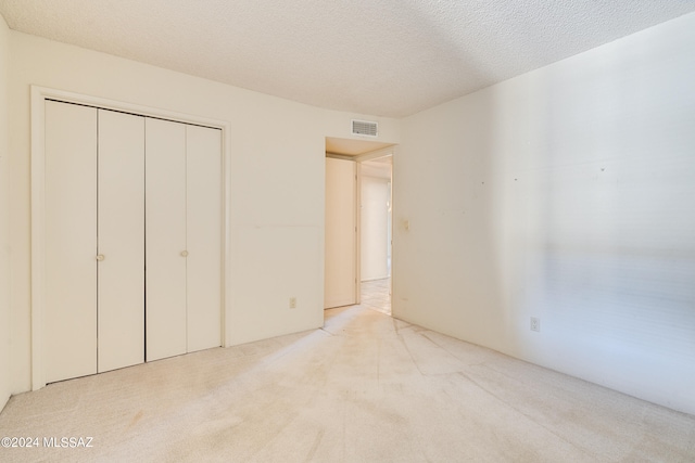 unfurnished bedroom with light carpet, a closet, and a textured ceiling