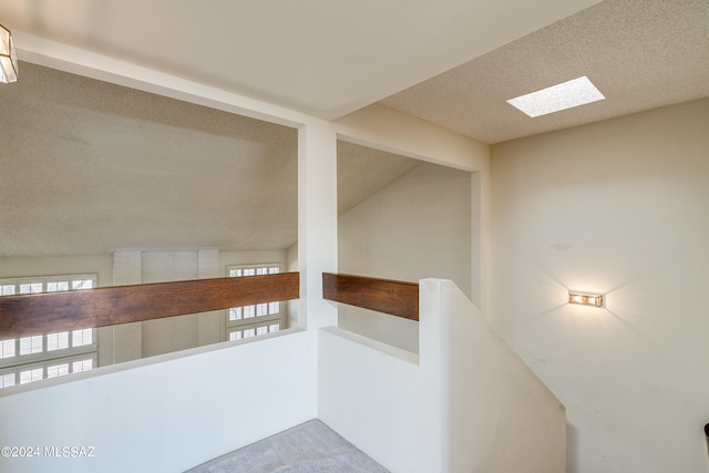 stairs featuring vaulted ceiling with skylight, a textured ceiling, and carpet floors