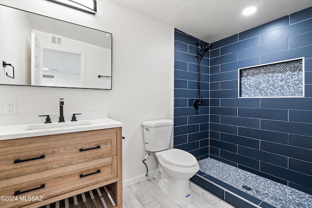 bathroom with a tile shower, vanity, and toilet