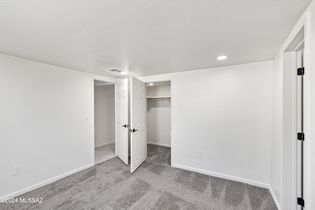 unfurnished bedroom with a walk in closet, a closet, and light colored carpet