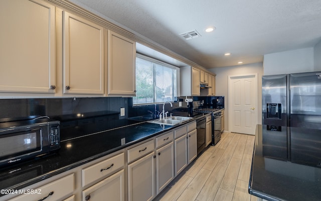 kitchen with cream cabinetry, dark stone counters, sink, black appliances, and light hardwood / wood-style floors