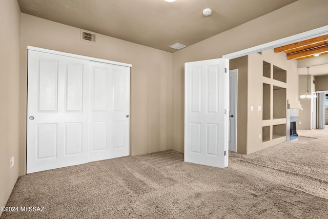 unfurnished bedroom with beam ceiling, an inviting chandelier, carpet flooring, and a closet