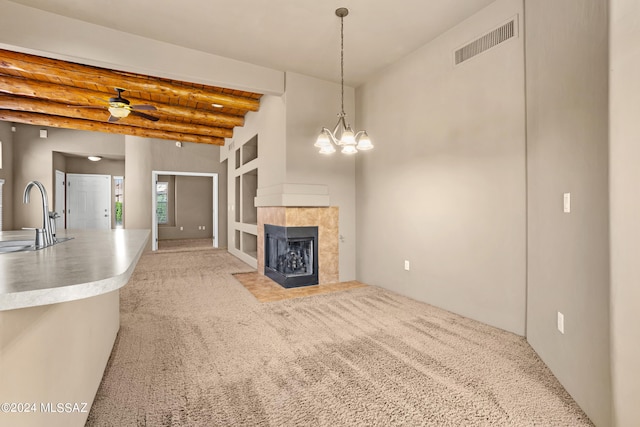 unfurnished living room with beam ceiling, a tile fireplace, ceiling fan with notable chandelier, sink, and light colored carpet