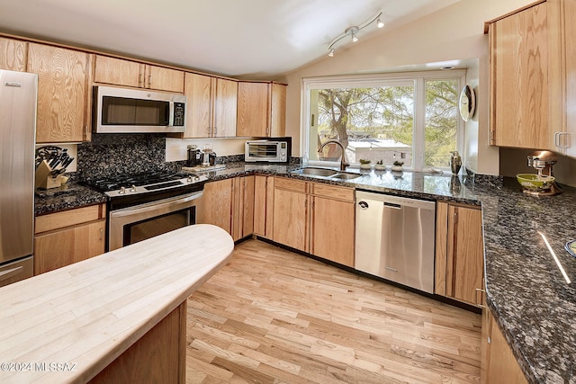 kitchen with appliances with stainless steel finishes, sink, light wood-type flooring, vaulted ceiling, and decorative backsplash