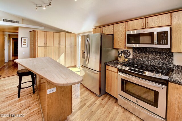 kitchen with vaulted ceiling, tasteful backsplash, appliances with stainless steel finishes, and light hardwood / wood-style flooring