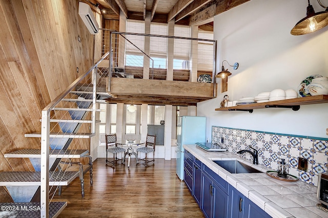 kitchen featuring dark hardwood / wood-style flooring, blue cabinetry, an AC wall unit, tile counters, and wooden walls