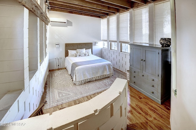 bedroom with beamed ceiling, hardwood / wood-style floors, and a wall mounted air conditioner