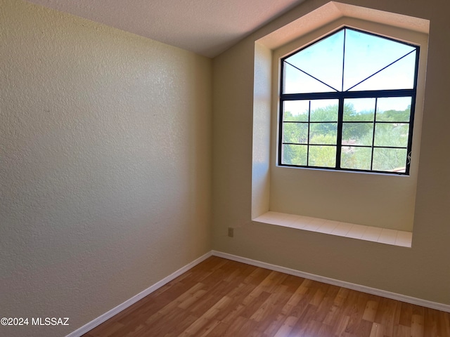 unfurnished room with a textured ceiling, wood-type flooring, and lofted ceiling