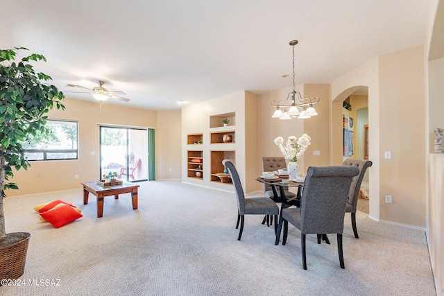 dining space with ceiling fan with notable chandelier, built in features, arched walkways, and light colored carpet