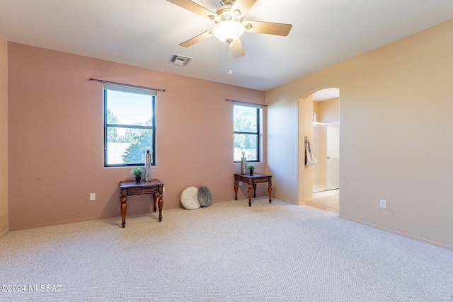 carpeted empty room featuring arched walkways, visible vents, a ceiling fan, and baseboards