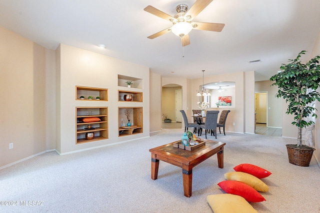 carpeted living area with arched walkways, built in features, baseboards, and a ceiling fan
