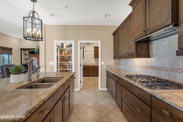 kitchen with stainless steel gas cooktop, backsplash, sink, pendant lighting, and light stone counters