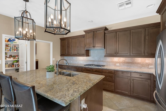 kitchen featuring a center island with sink, appliances with stainless steel finishes, light stone countertops, pendant lighting, and sink