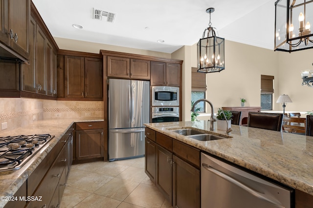 kitchen with sink, backsplash, stainless steel appliances, pendant lighting, and light stone counters