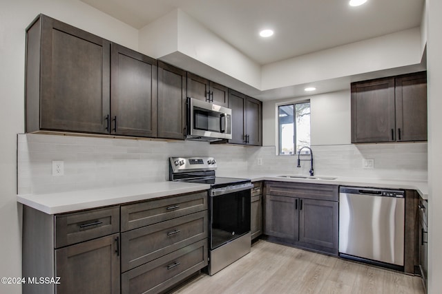 kitchen with backsplash, sink, light wood-type flooring, appliances with stainless steel finishes, and dark brown cabinetry