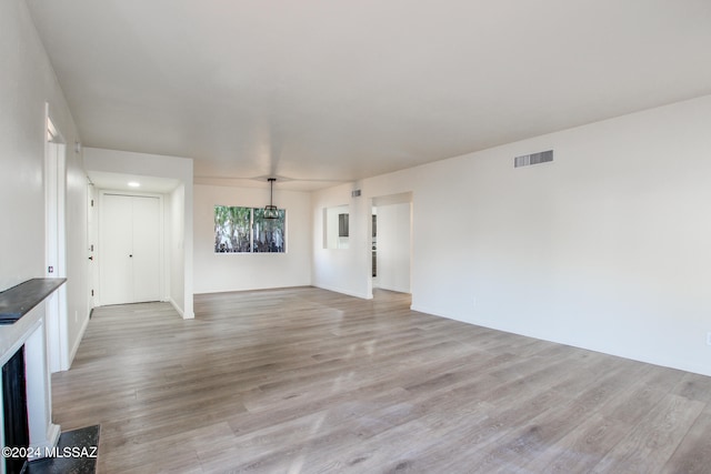 unfurnished living room featuring a chandelier and light wood-type flooring