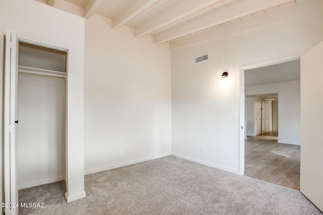 unfurnished bedroom featuring beam ceiling, light carpet, and a closet