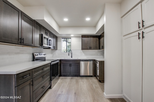 kitchen featuring decorative backsplash, appliances with stainless steel finishes, light wood-type flooring, dark brown cabinets, and sink