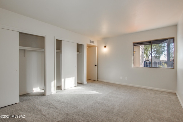 unfurnished bedroom featuring light carpet and two closets