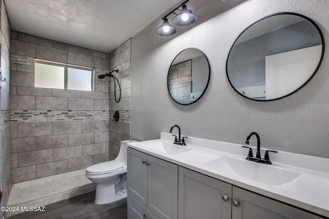 bathroom featuring vanity, a tile shower, wood-type flooring, and toilet