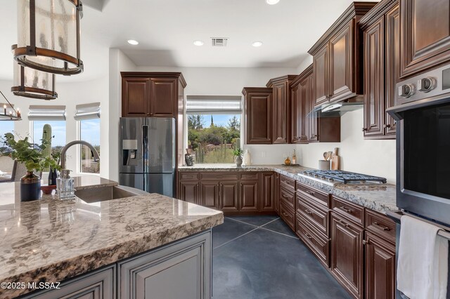 kitchen featuring sink, stainless steel refrigerator with ice dispenser, light stone counters, a breakfast bar, and a kitchen island with sink