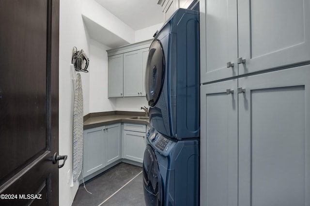 laundry area with sink, stacked washer / drying machine, and cabinets