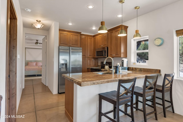 kitchen with kitchen peninsula, a breakfast bar area, hanging light fixtures, stainless steel appliances, and light tile patterned floors