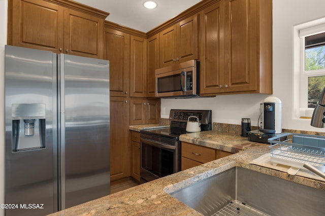 kitchen with stainless steel appliances, light stone countertops, sink, and tile patterned flooring