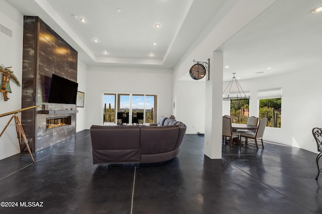 living room featuring a large fireplace, a chandelier, a tray ceiling, and a healthy amount of sunlight